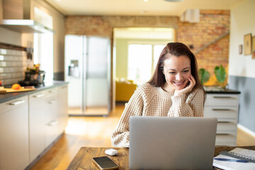 Young adult woman using a laptop in a kitchen