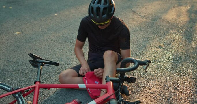 health care problem concept unhappy man wearing helmet sportswear opening first aid kit taking bandage as he is suffering from knee ache Health body care