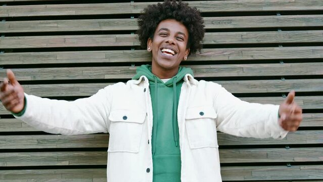 Happy funky generation z hipster rapper African American guy dancing, singing, having fun feeling hip-hop or rap vibe, moving and gesturing in slow motion standing at wooden wall outdoors.
