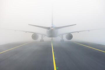 Airplane taxing on taxiway in white fog conditions. Yellow taxi line