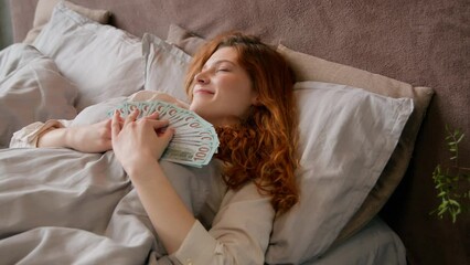 Caucasian happy woman sleeping in bed in luxury vacation with money rich wealthy girl businesswoman holding banknotes cash financial success sleep in bedroom lottery winning earnings income - Powered by Adobe