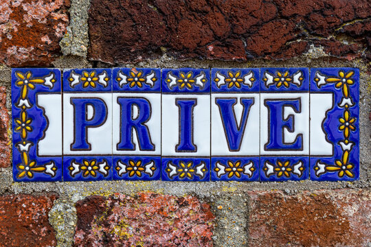 Spanish tile sign with the Dutch word Prive which means: Private, blue letters with white background and framed with small yellow flowers