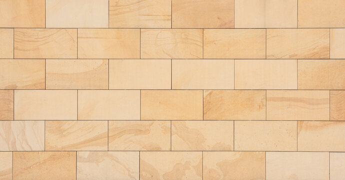 texture of a tiled beige stone wall as background, natural stone wall texture as background. Close-up of a wall clad in limestone