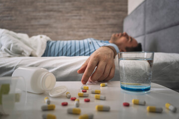 a man sleeps on a bed . table with pills and a glass of water. Sleeping pills for a good sleep. Man sleeping - pills on bed table. drug overdose. a lethal dose of the drug,