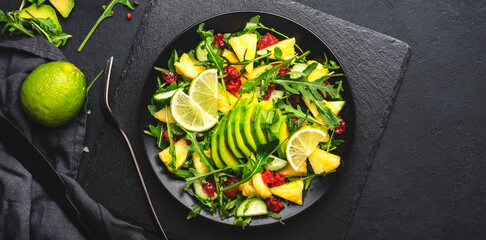 Vegan salad with fresh pineapple, arugula, avocado and dried cherry on black kitchen table, top...