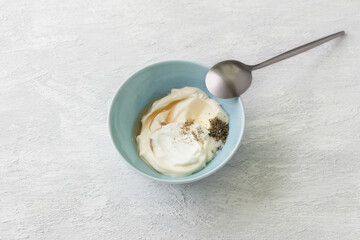 Blue bowl with salad dressing from sour cream, mayonnaise, wine vinegar and spices on a light gray background. Stage of cooking healthy vegan salad