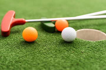 Mini-golf clubs and balls of different colors laid on artificial grass.