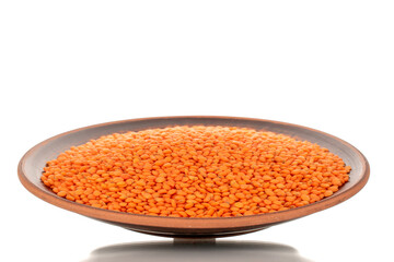 Red lentils on a clay dish, macro, isolated on a white background.
