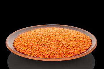 Red lentils on a clay dish, macro, isolated on a black background.