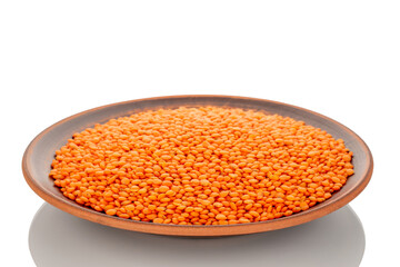 Red lentils on a clay dish, macro, isolated on a white background.
