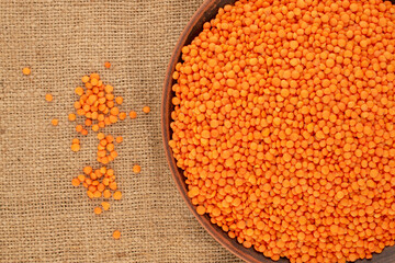 Red lentils on a clay dish on a jute cloth, macro, top view.