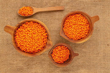 Red lentils in three wooden cups with a wooden spoon on a jute cloth, macro, top view.