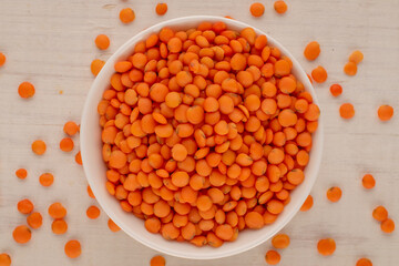 Red lentils in a white ceramic saucer on a wooden table, macro, top view.