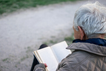 Fototapeta premium Old man with gray hair reading a book sited on an bench.