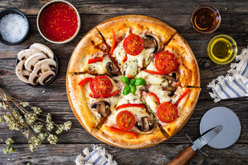 Circle vegetarian pizza with mozzarella cheese, mushrooms and tomatoes on wooden table
