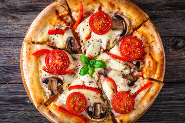 Circle vegetarian pizza with mozzarella cheese, mushrooms and tomatoes on wooden table
