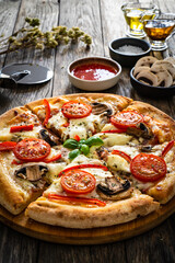 Circle vegetarian pizza with mozzarella cheese, mushrooms and tomatoes on wooden table
