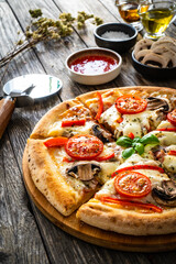 Circle vegetarian pizza with mozzarella cheese, mushrooms and tomatoes on wooden table
