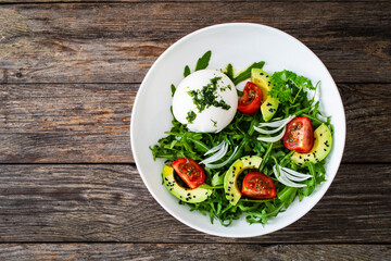 Burrata cheese with leafy greens, avocado and cherry tomatoes on wooden table
