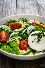 Burrata cheese with leafy greens, avocado and cherry tomatoes on wooden table
