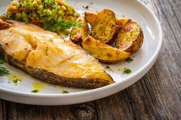Fish dish - fried halibut with baked potatoes and cabbage salad on wooden table