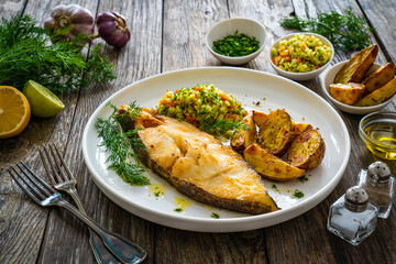 Fish dish - fried halibut with baked potatoes and cabbage salad on wooden table - obrazy, fototapety, plakaty