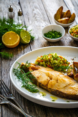 Fish dish - fried halibut with baked potatoes and cabbage salad on wooden table