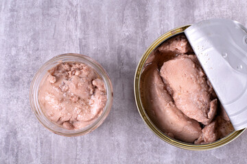 Canned cod liver with oil in bowl and open tin on gray table. Top view