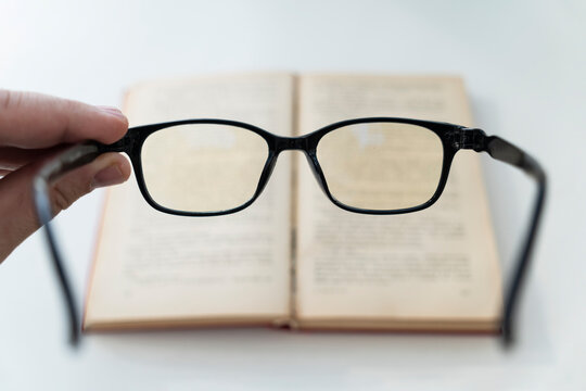book and eye glasses for read and write over blurred background with copy space, reading glasses in his hands on a blurry book background. poor vision concept. loss of vision,