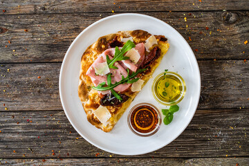 Pinsa Romana with mortadella, parmesan cheese and vegetables on wooden table
