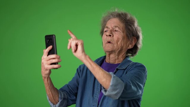 Funny crazy happy elderly old toothless woman taking selfie using mobile cell phone isolated on solid green screen background studio portrait. Slow motion