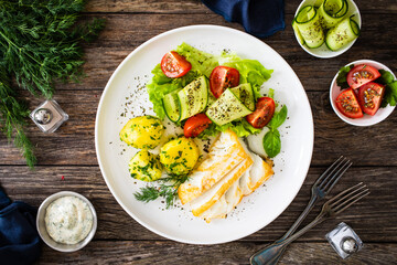 Fried halibut loin with boiled potatoes and fresh vegetables on wooden table

