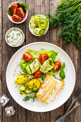 Fried halibut loin with boiled potatoes and fresh vegetables on wooden table
