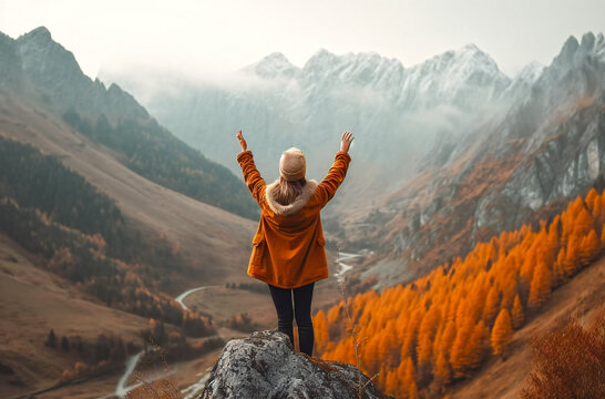 Beautiful mountains in fog and a standing young woman with arms raised