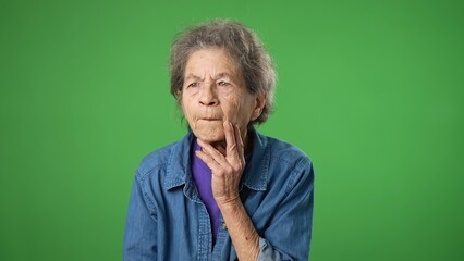 Portrait of thinking, smart puzzled pensive elderly senior old woman with wrinkled skin and grey hair looks around thinks with ideas raised finger thumbs up isolated on green screen background