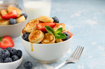 Trendy mini pancakes in a bowl with berries and honey. pancake. Healthy breakfast, snack, dessert. Copy space