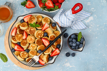 Trendy mini tiny pancakes in a red frying pan with berries and honey. Top view. Copy space