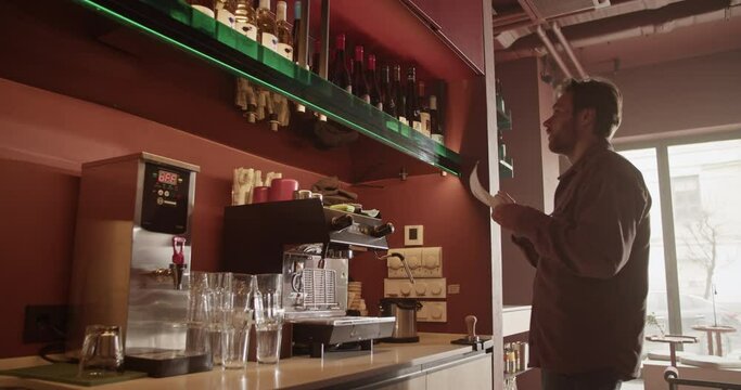 Male barkeeper checking quantity of alcohol bottles on shelves