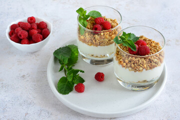 Two glasses of yogurt and granola with a bowl of fresh raspberries on the side  