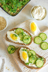 Cottage cheese sandwiches on whole grain bread with half an egg and cucumber on a wooden board on the table top view
