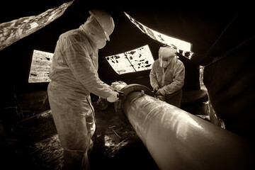 A worker in protective clothing performs a composite repair of a pipeline flange connection, black...