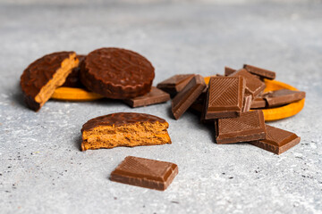 Chocolate bar pieces and cookies lying in a round wooden stands against a gray spotted background.