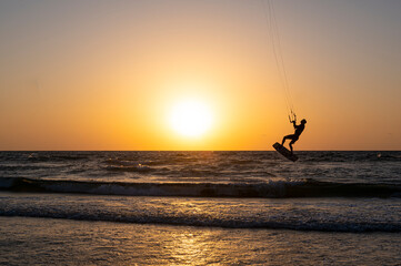 Black silhouette of a man on a wakeboard taking off over the Mediterranean Sea in Israel against the backdrop of sunset and horizon