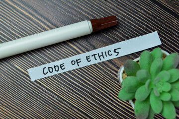 Concept of Code of Ethics write on sticky notes isolated on Wooden Table.