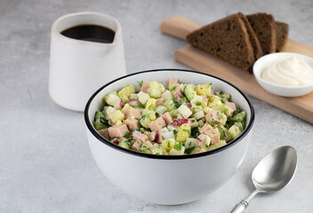Russian cold soup - okroshka with vegetables, sausage, herbs, kvass and black bread on a gray background.