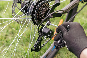 Mechanics Hand Repairing Bicycle in Bike Workshop. Closeup of Male Muscular Hand Examining and Fixing Modern Cycle Transmission System. Bike Maintenance and Sport Shop Concept