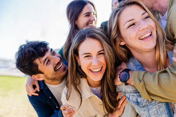 Diverse group of young adult friends having fun hugging each other outside. Joyful millennial people laughing enjoying time together. Community and friendship concept