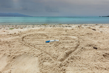 Fototapeta na wymiar Test de grossesse positif dans un coeur tracé sur le sable face au lagon turquoise de Polynésie