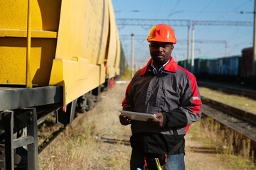 African american railway man with tablet computer at freight train terminal