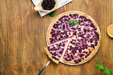 Shortcrust pastry tart with black сurrant and sour cream filling on a ceramic plate on a wooden background. Rustic style. blackcurrant recipes
